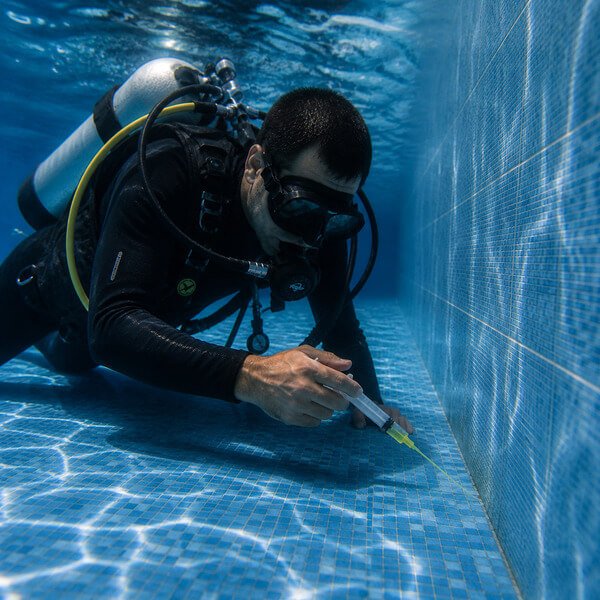 Mergulhador a realizar deteção de fugas em piscina com corante fluorescente junto a fissura no revestimento