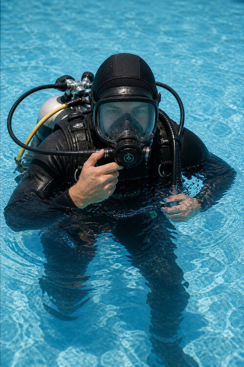 Mergulhador profissional com máscara integral a realizar deteção de fugas de água em piscina com equipamento subaquático