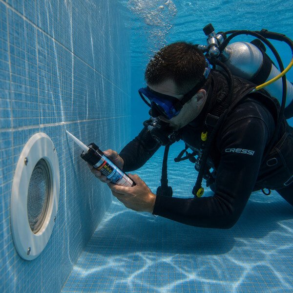 Mergulhador a reparar fuga em piscina com aplicação de selante subaquático junto a fissura na parede