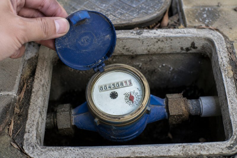 Mão de um proprietário a observar um contador da água para verificar uma possível fuga na canalização.