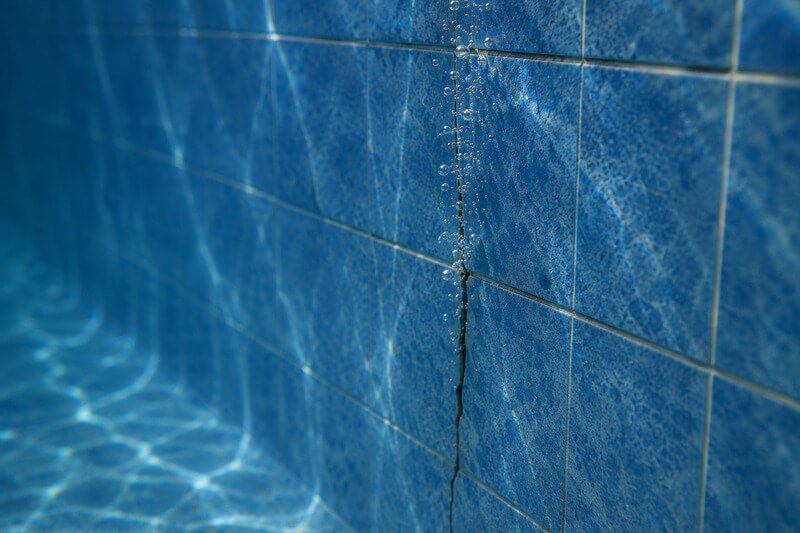 Pequena fissura na parede de uma piscina com bolhas de ar a indicar uma possível fuga de água.