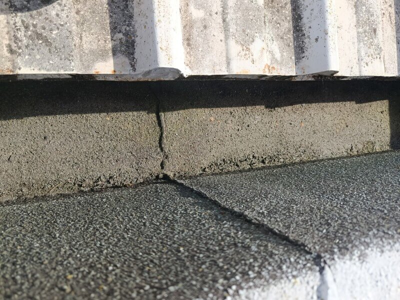 Fissura vertical no murete da cobertura, junto à impermeabilização, identificada durante a inspeção técnica como potencial ponto de entrada de água e origem da infiltração.