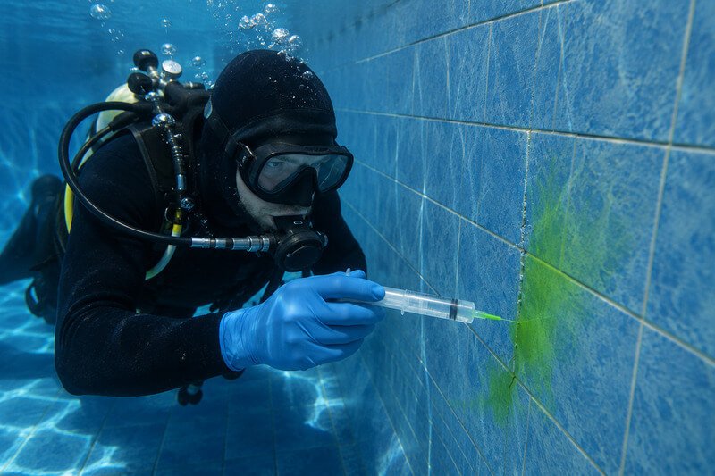 Mergulhador a injetar líquido corante numa fissura da piscina para localizar uma fuga de água.