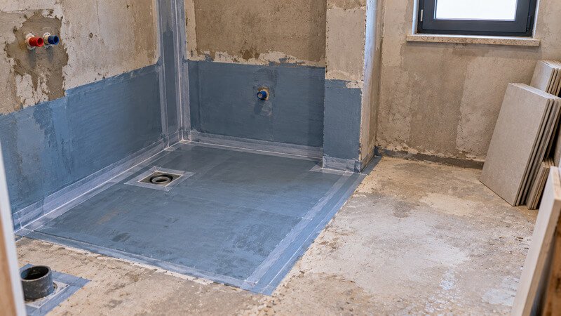 Profissional a observar manchas de humidade junto à base de duche enquanto o proprietário descreve quando surgem os sinais de infiltração
